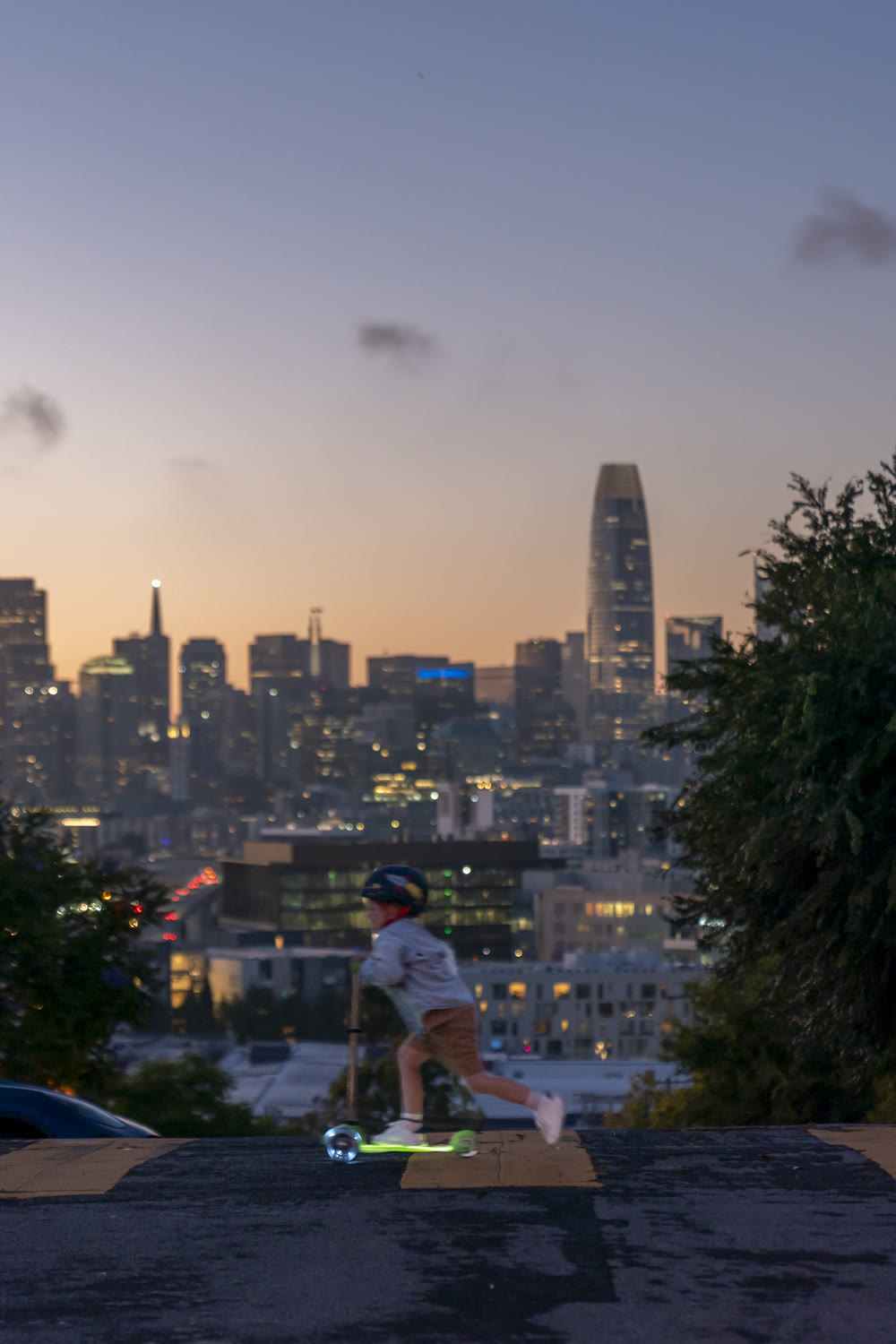 Kid riding a Micro Kickboard scooter with the San Francisco skyline at sunset